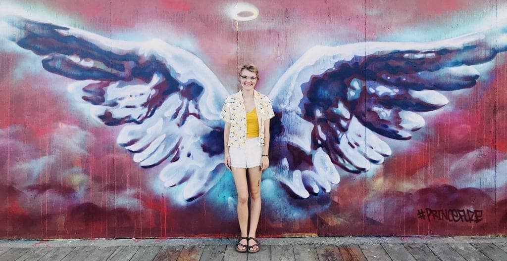Young adult woman standing near outdoor mural of angel wings painted on wall of building in Halifax