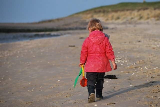 Child hiking on beach with shovel and pail in hand.