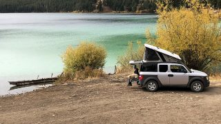 Grey truck camper with pop up tent parked at lake and available for rent near Yellowstone National Park