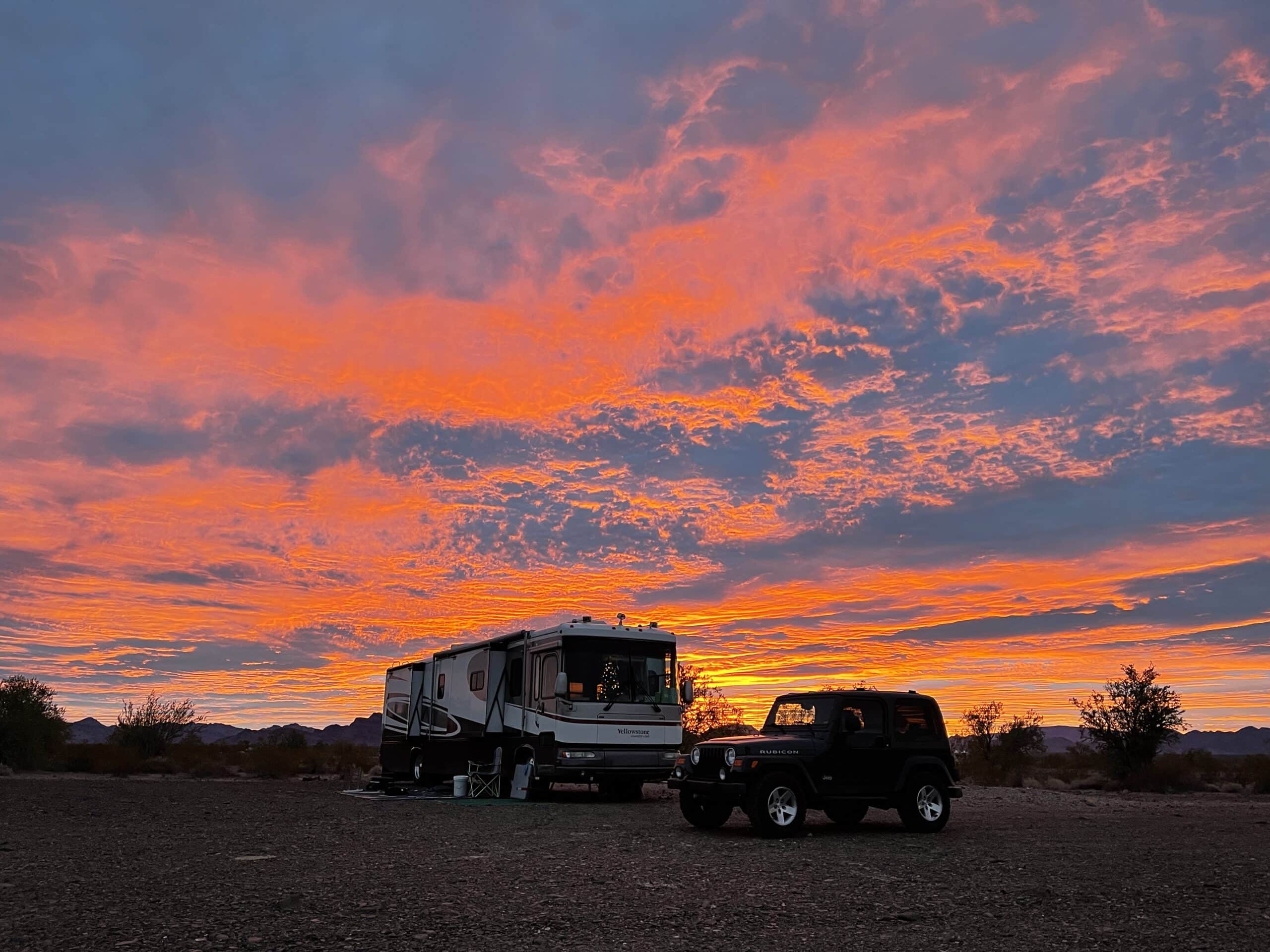 Jeep parked in front of large RV with orange sunset