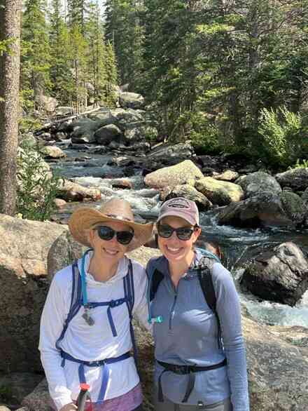 Two women on hike in front of river with backpacks and water filtration system.